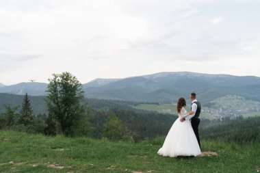 Düğün için. Gelin ve damat dağ yamacında koşuyorlar. Düğünden sonra. Beyaz gömlekli ve yelekli adam ve beyaz elbiseli bir kız dağlardaki yeşil arazide yürüyorlar.