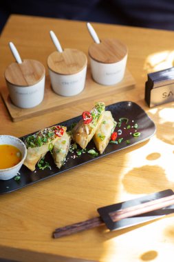 Tahta arka planda siyah tabakta karidesli Asya yemeği börekleri. Çeşitli baharat soslu pirinç kağıdında kızarmış börek. Üst görünüm, metin için boşluk