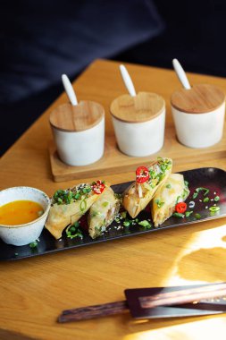 Tahta arka planda siyah tabakta karidesli Asya yemeği börekleri. Çeşitli baharat soslu pirinç kağıdında kızarmış börek. Üst görünüm, metin için boşluk