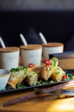 Tahta arka planda siyah tabakta karidesli Asya yemeği börekleri. Çeşitli baharat soslu pirinç kağıdında kızarmış börek. Üst görünüm, metin için boşluk