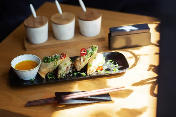 Asian food spring rolls with shrimps on black plate on a wooden background. Fried spring rolls in rice paper with a variety of spices sauce. Top view, space for text — Stock Photo, Image