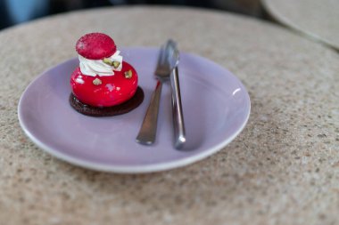 Mor tabakta izole edilmiş vişneli kremalı Fransız pastası. Çikolata ve makaron süslemeli kırmızı modern Avrupa tatlısı. Modern Avrupa pastası. Sığ odak