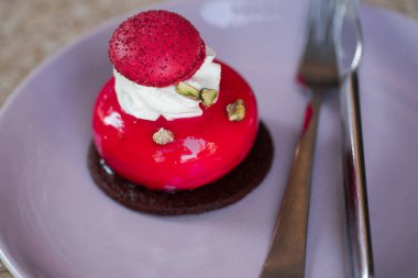 Mor tabakta izole edilmiş vişneli kremalı Fransız pastası. Çikolata ve makaron süslemeli kırmızı modern Avrupa tatlısı. Modern Avrupa pastası. Sığ odak