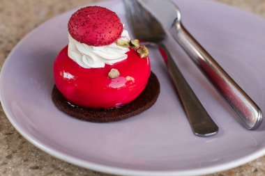 Mor tabakta izole edilmiş vişneli kremalı Fransız pastası. Çikolata ve makaron süslemeli kırmızı modern Avrupa tatlısı. Modern Avrupa pastası. Sığ odak