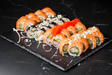 Siyah mermer arka planda servis edilen çeşitli suşiler. Japon yemeği için suşi menüsü. Japon suşi seti. Ton balığı, somon, karides, yengeç, havyar ve avokado. Yatay fotoğraf.