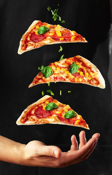 İnsanlar Elleri Üç dilim pizza alıyor. Pizza ve yemek konsepti. Ortadaki pizzaya odaklan. Açık hava partisi teması. Pizza ve sebzeleri siyah arka planda uçurmak. Dikey fotoğraf.