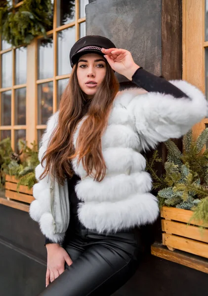Doğal kısa beyaz kürk giyen güzel beyaz kadın Noel vitrininin yanındaki bir portre için poz veriyor. Noel dekoru. Moda. Tarz. Doğal kürkten yapılmış kışlık giysiler. Dikey