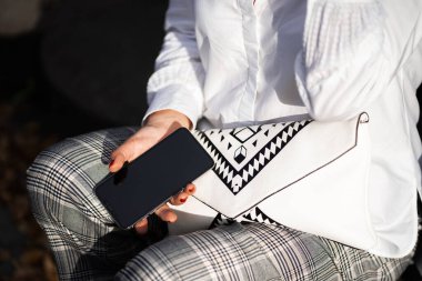 Çekici kız hafta sonu doğada dinleniyor. Parkta oturan beyaz gömlekli kız. Kafkas esmer, genç bir kadın dışarıda akıllı telefondan konuşuyor. Teknoloji ve aletler. Yatay.