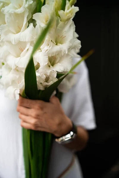 Молода жінка в білому одязі тримає букет. Квітковий магазин Букет квітів. Флорист. Композиція з білими квітами гладіолусів. Концепція квіткового магазину. Робота флориста. копіювання простору — стокове фото