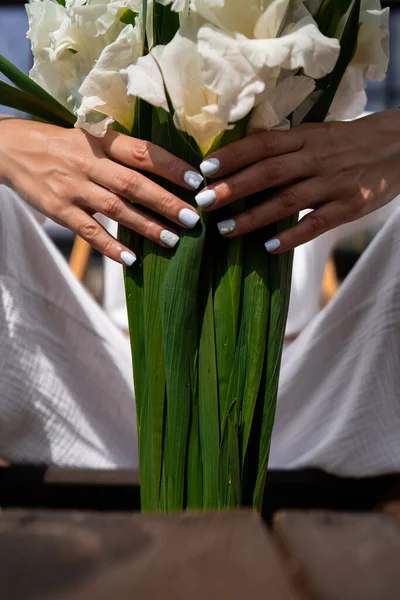 Mujer joven con ropa blanca sosteniendo ramo. Floristería Ramillete de flores. Florista. Arreglo con flores de gladiolo blanco. El concepto de una floristería. Florista de trabajo. espacio de copia —  Fotos de Stock