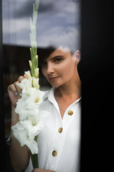 Vacker kvinna med kort brunett hår i vita kläder. Modefotografering. Mode modell poserar med blommor på mörk bakgrund. — Stockfoto