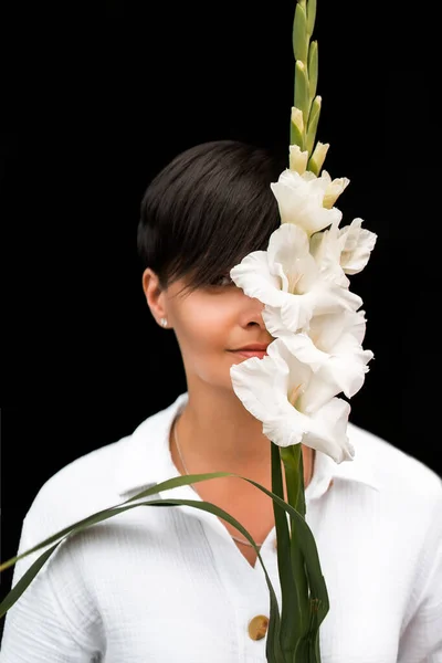 Красива жінка з коротким волоссям брюнетки в білому одязі. Модна фотографія. Модна модель позує з квітами на темному тлі . — стокове фото