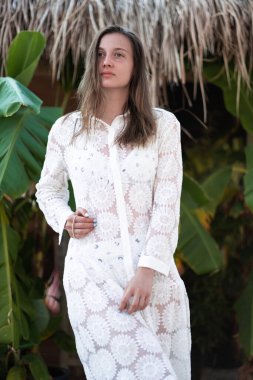 Kumsalda poz veren beyaz plaj elbiseli güzel esmer bir kız. Palm 'ın yanında duran kız. Modaya uygun. Manzaralı. Yaz