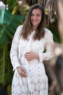 Kumsalda poz veren beyaz plaj elbiseli güzel esmer bir kız. Palm 'ın yanında duran kız. Modaya uygun. Manzaralı. Yaz