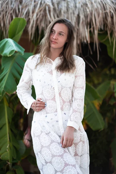 Una hermosa chica morena en vestido de playa blanco posando en la playa. Chica de pie cerca de la palma. vista look.top de alta moda. Verano — Foto de Stock