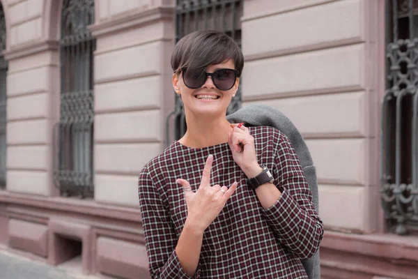 Moda de outono ao ar livre. A menina morena com cabelo curto em casaco cinza elegante e óculos de sol, posando no fundo do edifício. Rua fashion.Autumnal estilo de vida — Fotografia de Stock