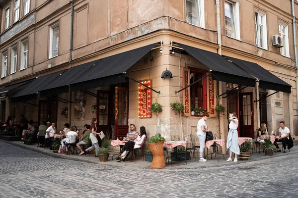 LVIV, UKRAINE - október 13, 2019 View of street with tables of cafe in European country. Kényelmes városkép Lviv-ről. Építészet és műemlékek. Képeslap. Az emberek pihennek és pihennek egy gyönyörű étteremben. — Stock Fotó