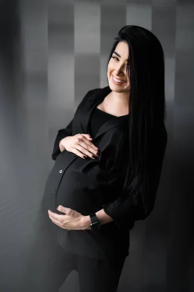 Femme enceinte en vêtements noirs tient la main sur le ventre sur un fond lumineux. Grossesse, maternité, concept de préparation et d'attente - gros plan de la femme enceinte heureuse avec un gros ventre à la fenêtre . — Photo