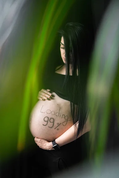Mujer embarazada en ropa negra toma de la mano en el vientre con la carga de inscripción 99. El embarazo, la maternidad, la preparación y el concepto de expectativa - primer plano de la mujer embarazada feliz con vientre grande. . —  Fotos de Stock