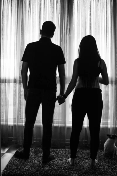 Romantic couple expecting baby, holding hands and touching foreheads while standing together against window at home . Pregnancy, maternity, preparation and expectation concept. black white photo — Stock Photo, Image
