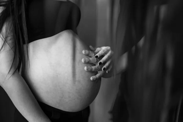 Pareja romántica esperando un bebé, tomados de la mano y tocando la frente mientras están de pie juntos en el vientre contra la ventana en casa. Concepto de embarazo, maternidad, preparación y expectativa. primer plano — Foto de Stock