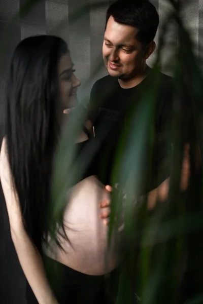 Casal romântico esperando bebê, de mãos dadas e tocando na testa enquanto estão juntos na barriga contra a janela em casa, espaço livre. Conceito de gravidez, maternidade, preparação e expectativa . — Fotografia de Stock