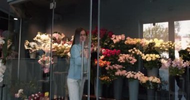 Çiçek teslimatı. Çiçekçi kız gülleri alıp buket yapıyor. Çiçekçi dükkanı konsepti. Farklı çeşitlerde taze bahar çiçekleri buzdolabı odasında çiçekler için. 4k