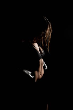 Karanlık ringde kadın boksör eğitimi. Ağır çekim. Siluet. Boks konsepti. Dövüşçü kadın yumruğunu sık. Seyirci video boks maçı. Spor salonunda eldivenlerle gülümseyen kız boksu..