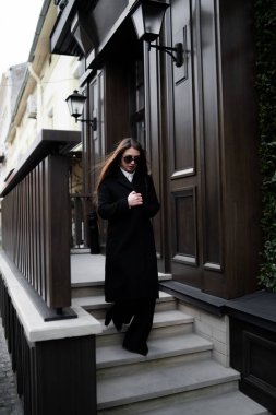 Soğuk bir sonbahar gününde esmer bir kadının sokakta yürürken çekilmiş fotoğrafı. Moda tarzı sokak portresi. Koyu renk günlük pantolon giyiyor.,