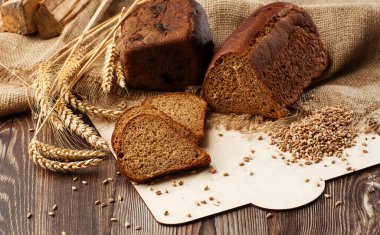 Üçgen şeklinde ekmek ve dikenli buğday başaklarının yanında ayçiçeği tohumları eski, yıpranmış ahşap masada yatıyor. Kırsal ekmek ve buğday eski bir tahta üzerinde