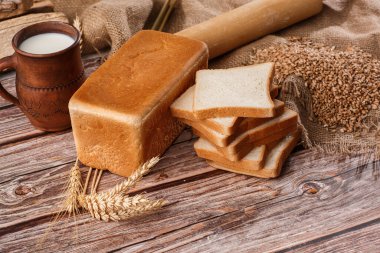 Ev yapımı ekmeğin yakın çekimi. Köylü karesi ekmek ve yazı için yeri olan buğday dikenleri. Ev yapımı pişirme. Unlu beyaz ekmek ve tahtadan kesilmiş süt.