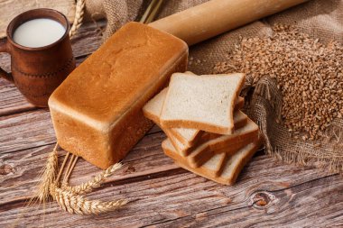 Ev yapımı ekmeğin yakın çekimi. Köylü karesi ekmek ve yazı için yeri olan buğday dikenleri. Ev yapımı pişirme. Unlu beyaz ekmek ve tahtadan kesilmiş süt.