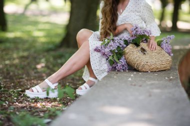 Kız elinde çiçekli bir hasır sepet tutuyor. Leylak dolu sepet. Kız ve çiçekler. Elinde bir sepet leylakla yürü. Çiçek.