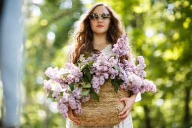 Beyaz elbiseli kız elinde çiçekli bir hasır sepet tutuyor. Leylak dolu sepet..