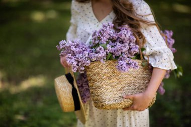 Kız elinde çiçekli bir hasır sepet tutuyor. Leylak dolu sepet. Kız ve çiçekler. Elinde bir sepet leylakla yürü. Çiçek.