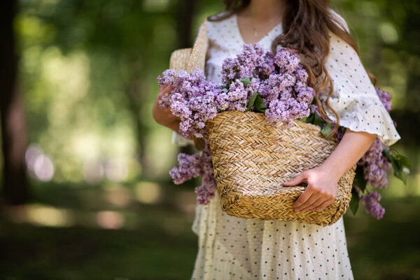 The girl holds in her hands a wicker basket with flowers. Basket with lilacs. Girl and flowers. Walk with a basket of lilacs in the hands. Floristics