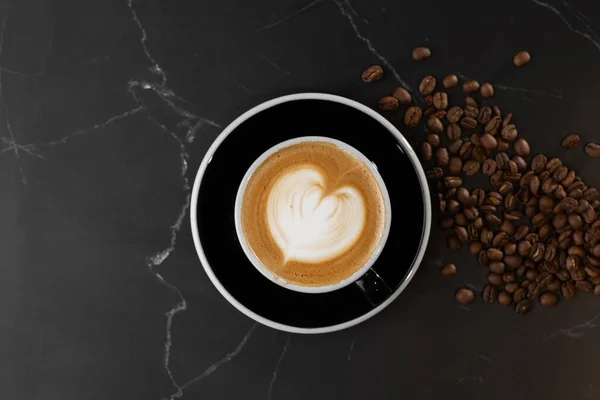 Tazza di caffè latte caldo con bella schiuma di latte latte texture art con chicco di caffè su sfondo di marmo nero. Vista aerea, copiare spazio. Pubblicità per il menu del caffè. Menù caffetteria. — Foto Stock