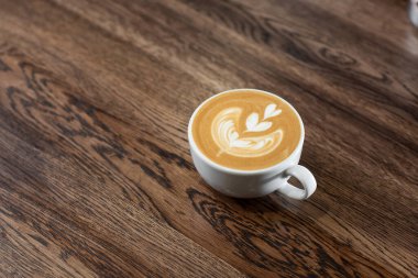 White cup of hot latte coffee with beautiful milk foam latte art texture isolated on wooden background. Overhead view, copy space. Advertising for cafe menu. Coffee shop menu.