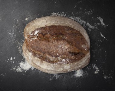 Bütün ekmek somun ve koyu arka plan üzerinde dağınık beyaz un