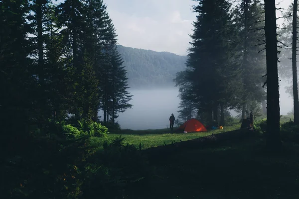 Foggy matin dans la forêt, des rayons de lumière illuminent la tente de camping, surplombant le lac — Photo