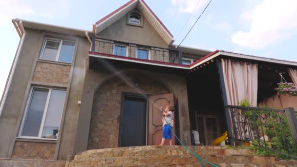 Niño jugando con agua de la manguera de agua en el patio trasero de la casa en el verano . — Vídeos de Stock