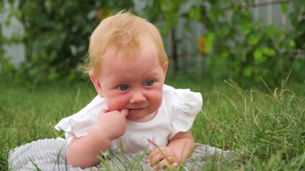 子寄生虫背景 赤ちゃんの歯が生えるの背景 屋外笑顔青い目の少女 赤ちゃんの歯が生えるの問題 赤ちゃんは 緑の草の上に横たわる 子供は庭で遊んでいます 歯を刈ってください — ストック動画