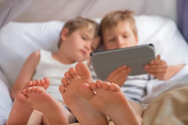 Dos niños sosteniendo el teléfono inteligente, tableta sentada en la silla, se centran en los pies de los niños . —  Fotos de Stock