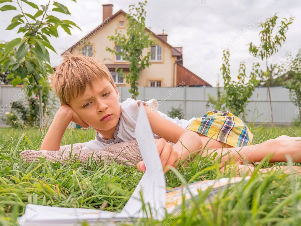 Kid with the book on the grass. Boy reading outside. Summer time spanding. Pre-schooling background. Reading outdoor. Book and nature.