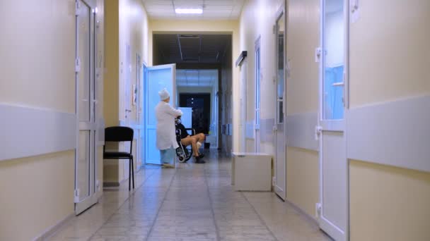 Male with leg burns on a wheelchair at hospital. View of a hospital hall. People in a clinic hall, walking. Medical facility. Hospital, clinic, private clinic. Medical reform. Pharmaceutical industry — Stock Video