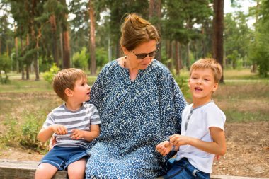 İki sevimli erkek hemşire ile konuşuyor, büyükanne. Park, Bahçe, orman gülüyor çocuklar. Bir ebeveyn ailesi. Kardeşler aşk. Kardeşler konuşuyor. Mutlu çocuklar arka plan. Aile ilişkileri.