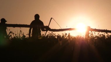 Köyde genç çiftçi siluetorak tırmık tırmık aracı yeşil yaz ayakta. Arka ışıkta büyük manuel hasat tırmık. Arka planda çayır lı tırplı bir adamın portresi