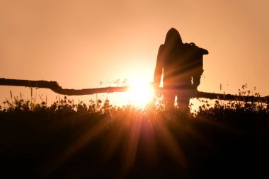 Sırt çantası arka ışıklı bir köyde bir adamın silueti. Arka ışıkta büyük manuel hasat tırmık. Arka planda bir çayır ile sırt çantası ile bir adamın portresi