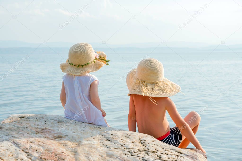 Little tourists near the sea. Vacation with children. Sunny summer days. Children on the seashore. Beautiful children looking to ocean. Happy childhood concept. Siblings, psyhology. Family vacation.