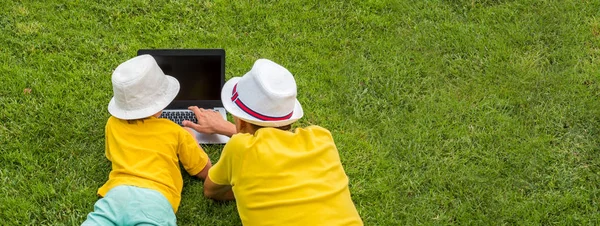 Father and son with notebook on sunny summer day. New approach to education. Back view of two boys with laptop lying on backyard. Happy summer sunny days. Boys in bright T-shirts spending time outdoor — Stock Photo, Image